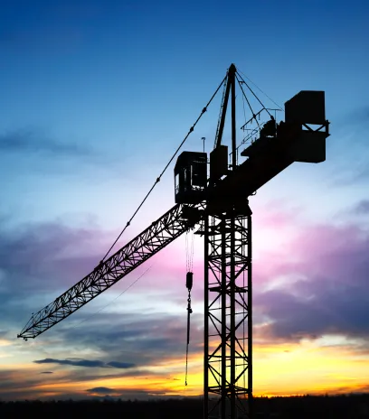 Silhouette of a construction crane against a colorful sunset sky.
