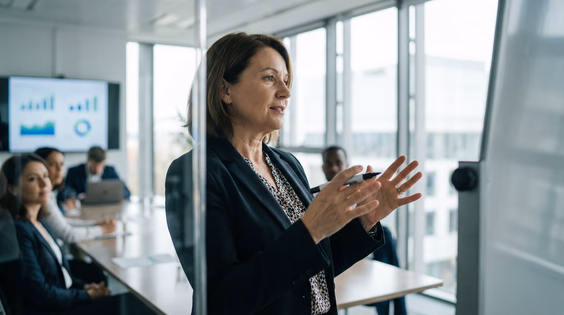 Businesswoman giving a presentation in a modern conference room with colleagues listening.