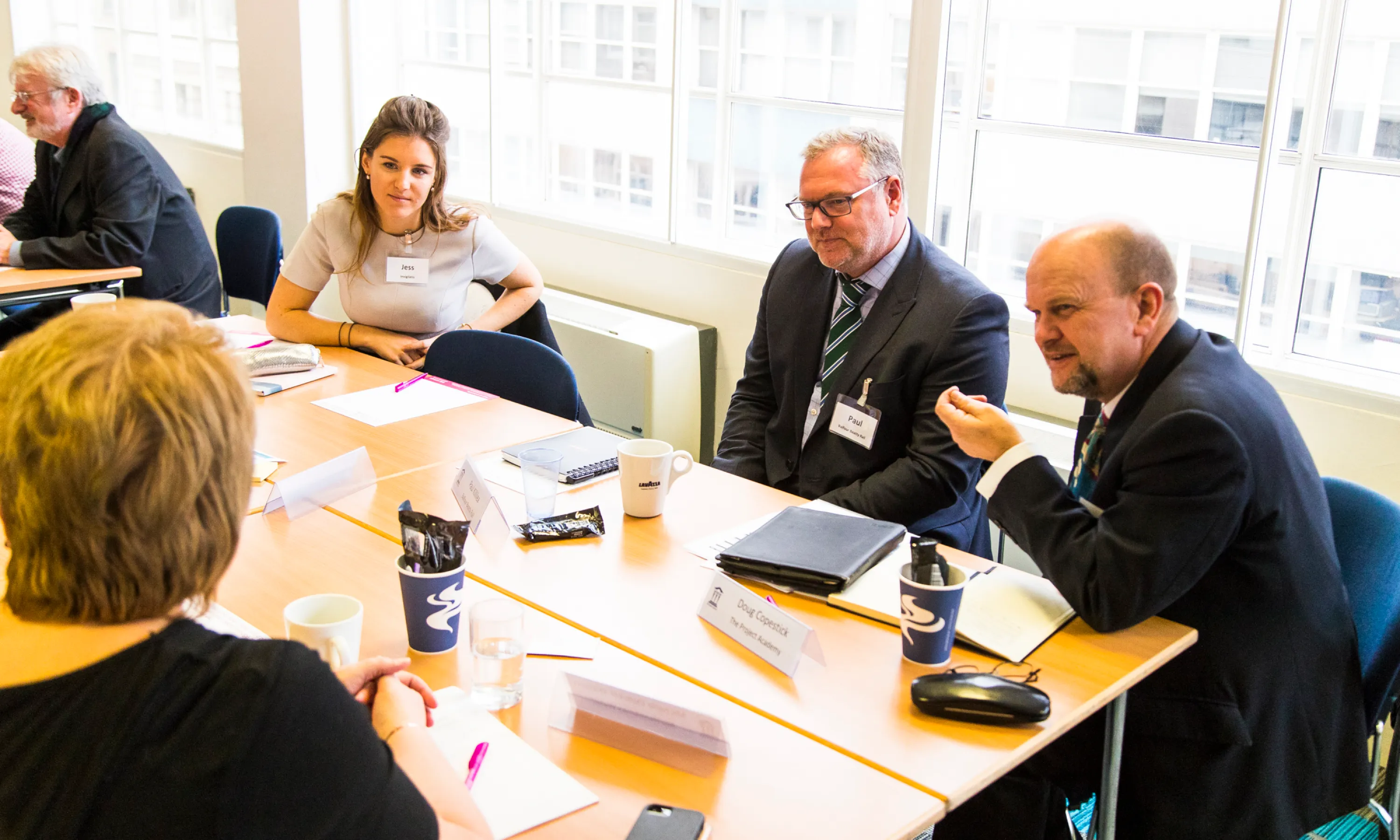 Four professionals in a business meeting sitting around a table with documents and coffee cups.
